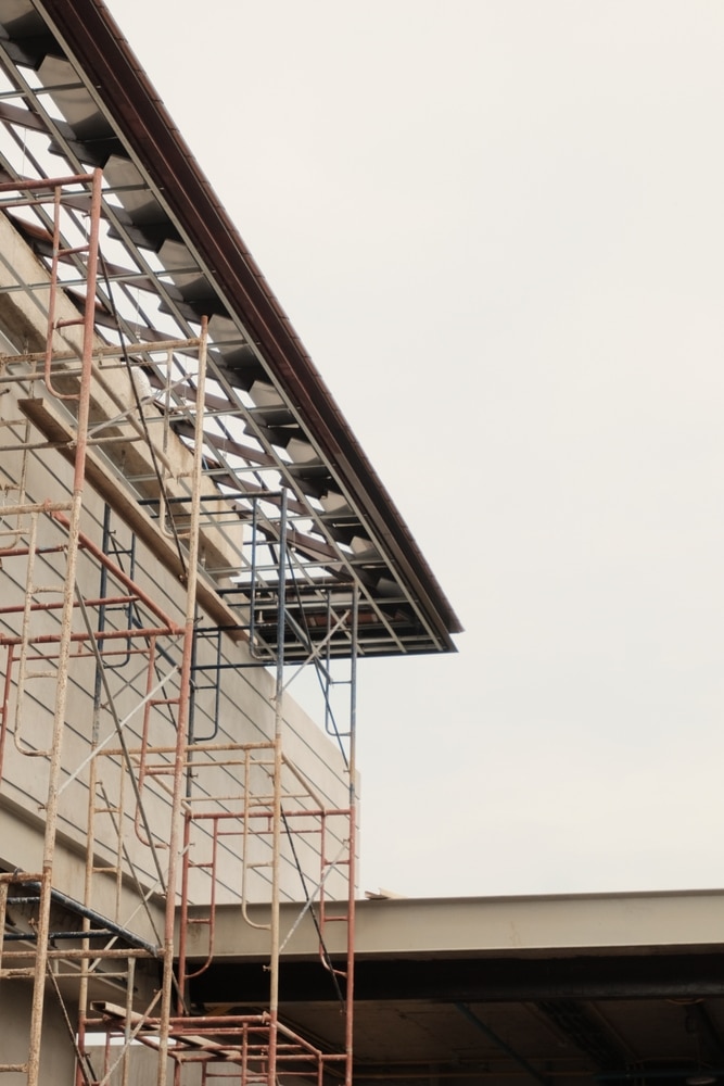 Échafaudage métallique rouillé devant la façade d'un bâtiment en construction. Vue détaillée de la charpente de toiture inachevée.
