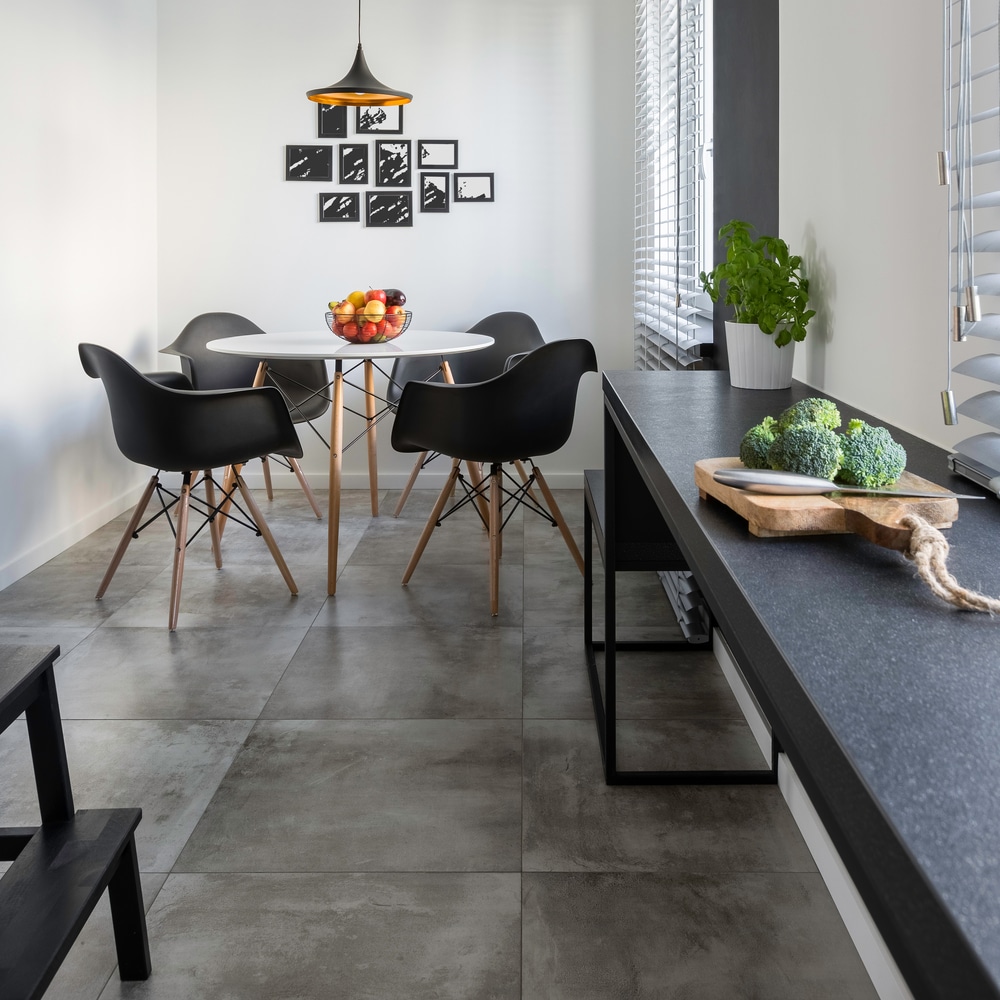 Coin repas moderne noir et gris avec chaises design Coin repas moderne. Table et chaises design noires, mur de cadres. Comptoir de cuisine sombre, brocolis frais, carrelage gris béton.