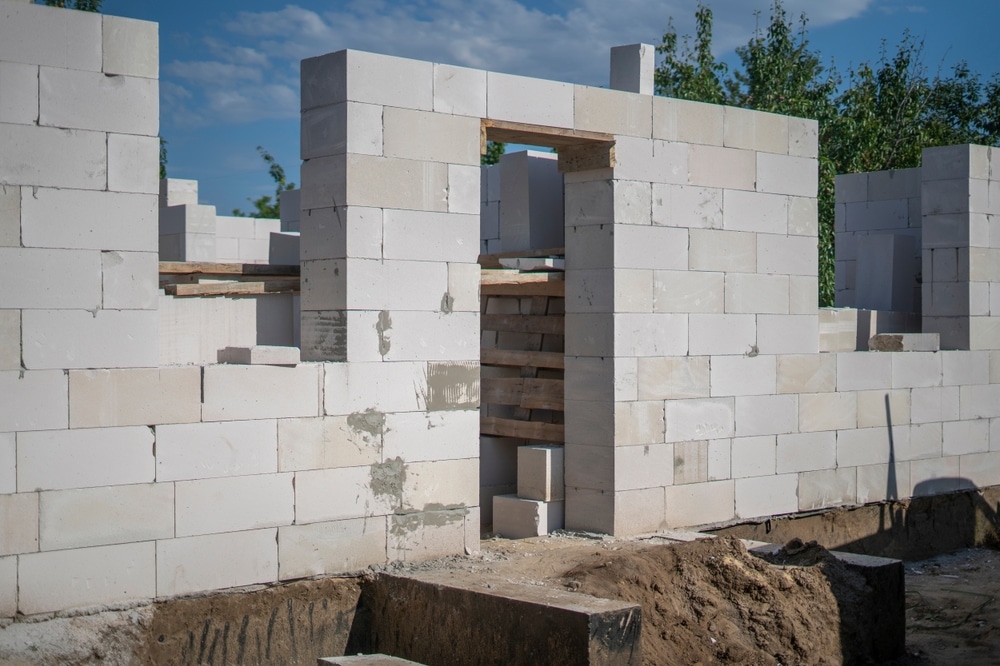 Murs porteurs en construction de blocs de béton cellulaire blancs. Vue sur les ouvertures de porte et de fenêtre, supports en bois, et fondation.