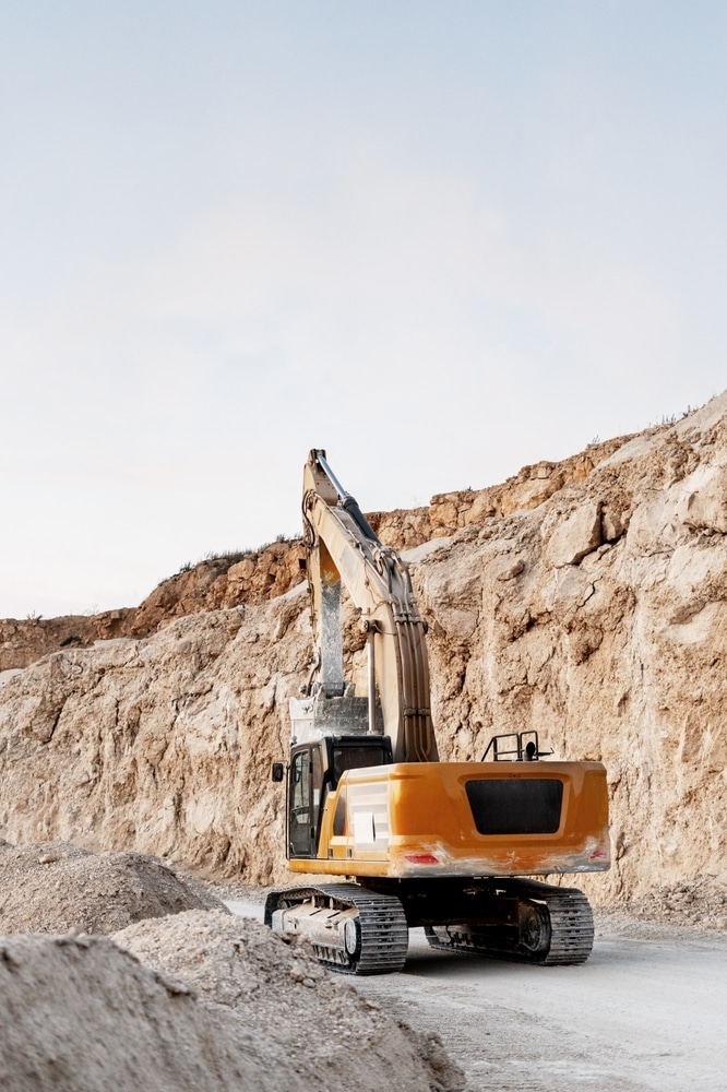 Pelleteuse carrière : l'engin de construction face à la roche. Puissante pelleteuse jaune au repos sur une route de carrière. Gros plan sur l'engin face à d'impressionnantes falaises calcaires.
