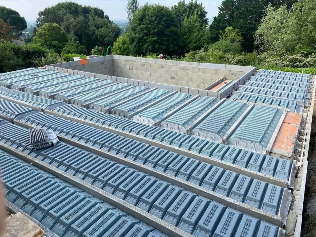 Chantier : plancher en construction avec rangées de coffrages (entrevous) isolants bleus sur poutrelles béton. Murs en parpaings.