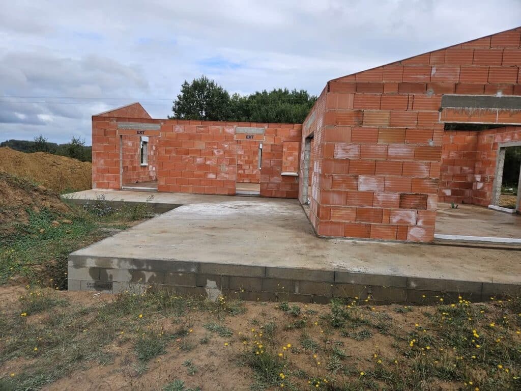 Structure d'une maison en construction: murs en briques thermiques rouges sur fondation en parpaings. Ouvertures de portes/fenêtres (EXT).