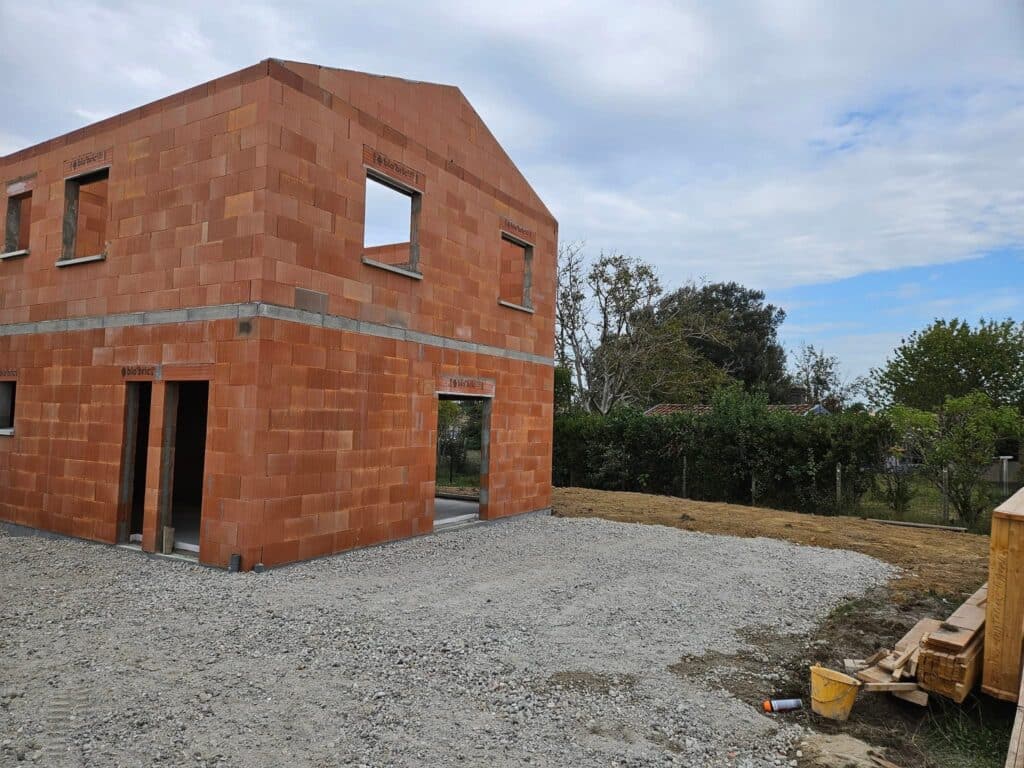 Gros œuvre : construction maison neuve briques bio'bric. Gros œuvre d'une maison neuve en briques terre cuite bio'bric, deux étages. Façade et ouvertures sur un chantier extérieur en gravier.