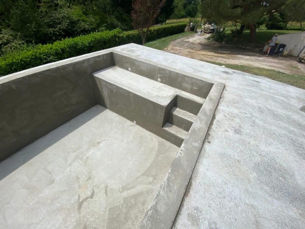 Construction piscine béton : enduit et banc immergé. Piscine contemporaine en béton fraîchement enduit. Escalier et banc immergé, structure prête pour la finition. Chantier extérieur.