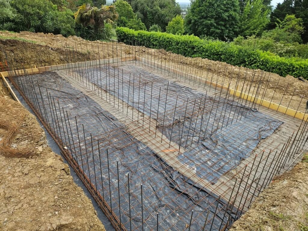 Ferraillage de la fondation : préparation de la dalle de piscine Préparation d'une fondation de piscine dans une excavation. Treillis soudé, rebarres verticales et membrane noire posés sur la base.