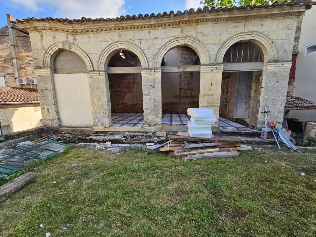 Restauration loggia en pierre : chantier et isolation du sol. Loggia en pierre ancienne à quatre arches en cours de rénovation. Le sol est préparé avec des panneaux d'isolation et du treillis.